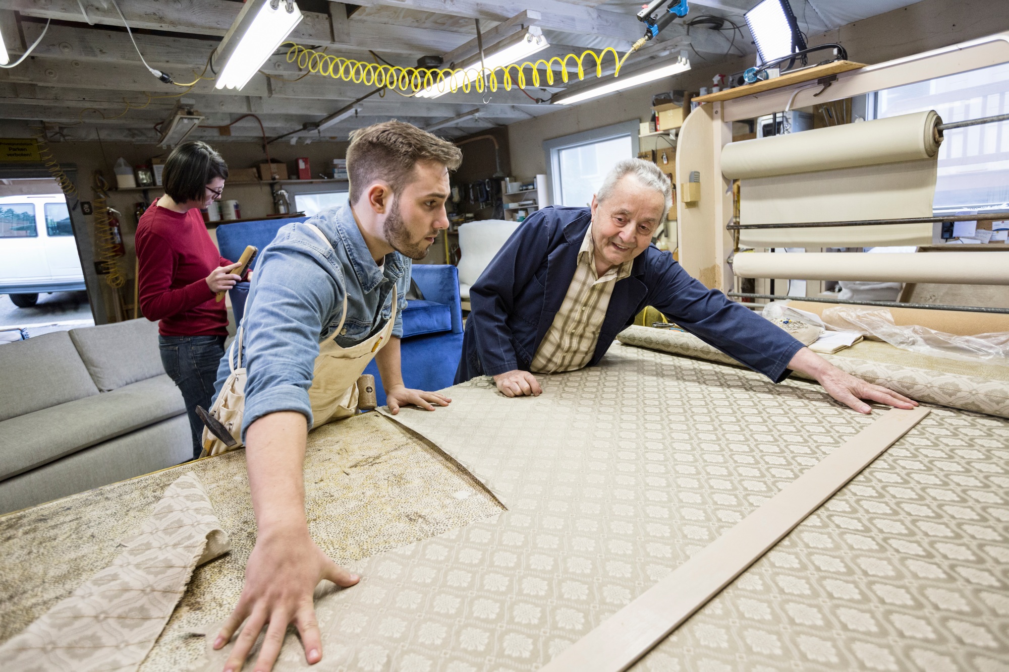 Young Caucasian man learning the art of upholstery from a senior male upholsterer.